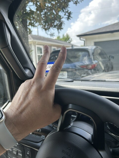 A driver making the familiar two-finger Jeep wave beside the steering wheel
